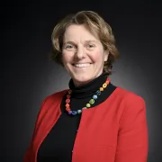 headshot of woman in a red jacket against a dark background