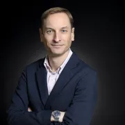 headshot of man in dark suit against black background