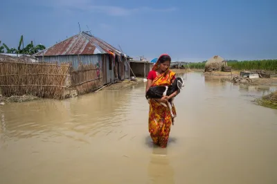 a woman in a sari carrying a goat as she walks through a flooded village