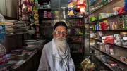 An elderly man sits in his small shop