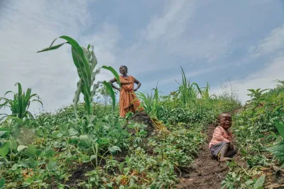 an african woman standing in a field with her hands on her hips with a child at her feet
