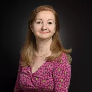 headshot of woman in pink against dark background