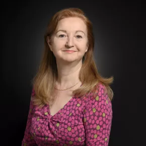 headshot of woman in pink against dark background