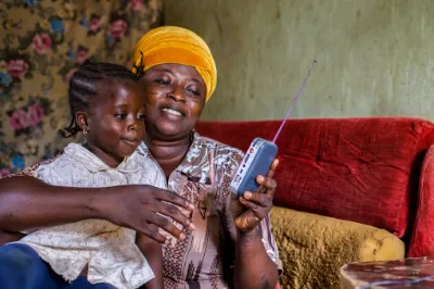 a mother and young daughter sit on a sofa listening to a portable radio
