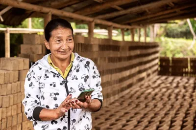 An older woman holds a mobile phone while smiling at something off camera 