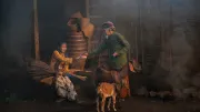 A rural couple and their goat in Indonesia sit in a dark barn