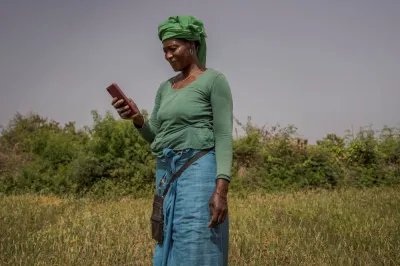 A Senegalese woman farmer in a field looking down at her phone
