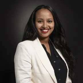 headshot of woman in white jacket against dark background