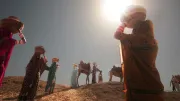 Women walk up a sand dune carrying baskets on their heads
