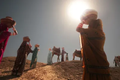 Women walk up a sand dune carrying baskets on their heads