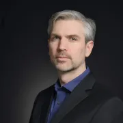headshot of man in dark suit against black background