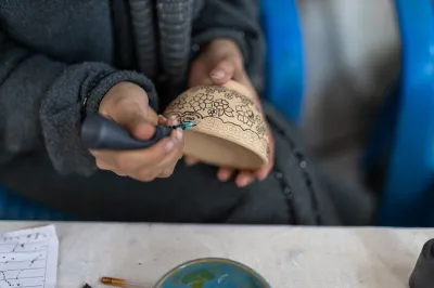 a woman decorates a clay bowl with black ink