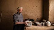 A man in a ceramic workshop holds dishes