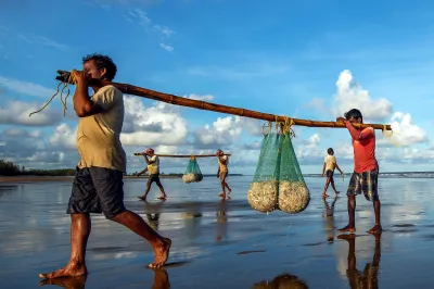 Fishermen walk the beach with their catch in India